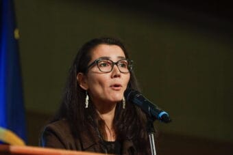 A woman in a black suit jacket speaking into a microphone.