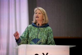 A woman in a kuspuk speaks at a podium.