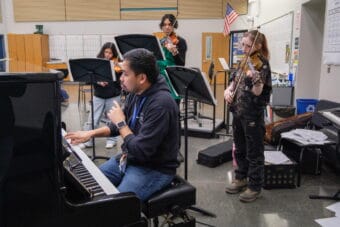 Serjoe Gutierrez sits at a piano to work with his first violinists to focus on intonation.